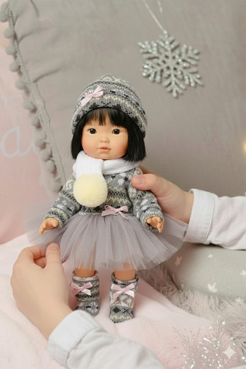 Asian Doll wearing a winter outfit with a hand holding it, against a soft background.