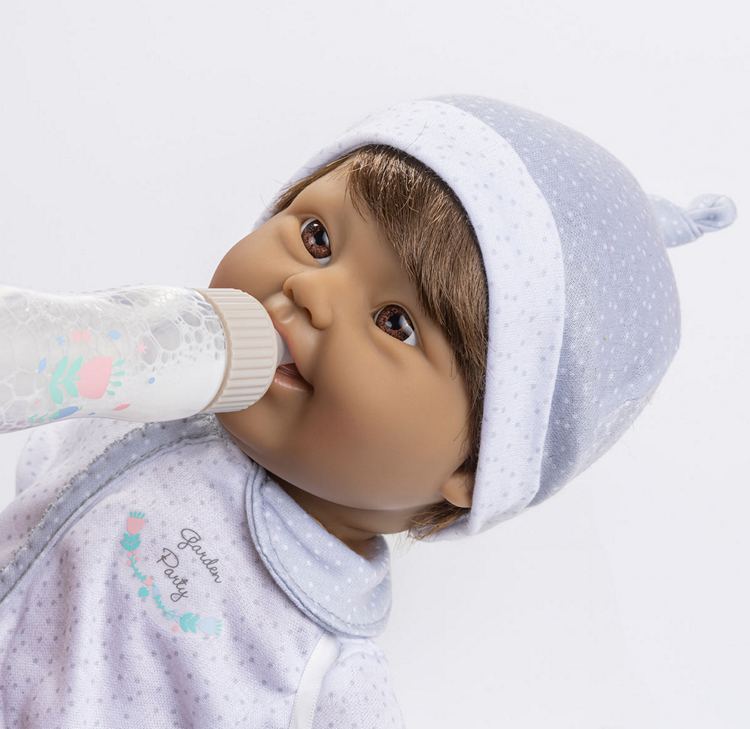 Down Syndrome Baby doll wearing a white hat and outfit, Drinking from a pretend bottle