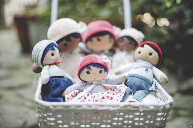 A wicker basket filled with various Kaloo Brand Soft, Safe Rag Dolls
