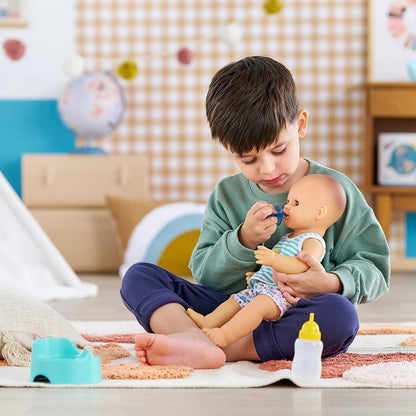 Young boy playing with Corolle Baby Paul potty training doll holding doll and pacifier with teal potty chair and bottle on floor