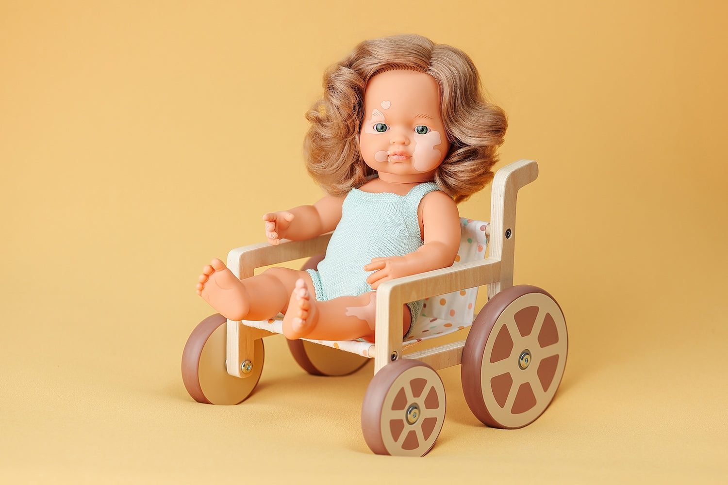 A Miniland educational 15 inch Vitiligo doll shown in the new doll's wheelchair