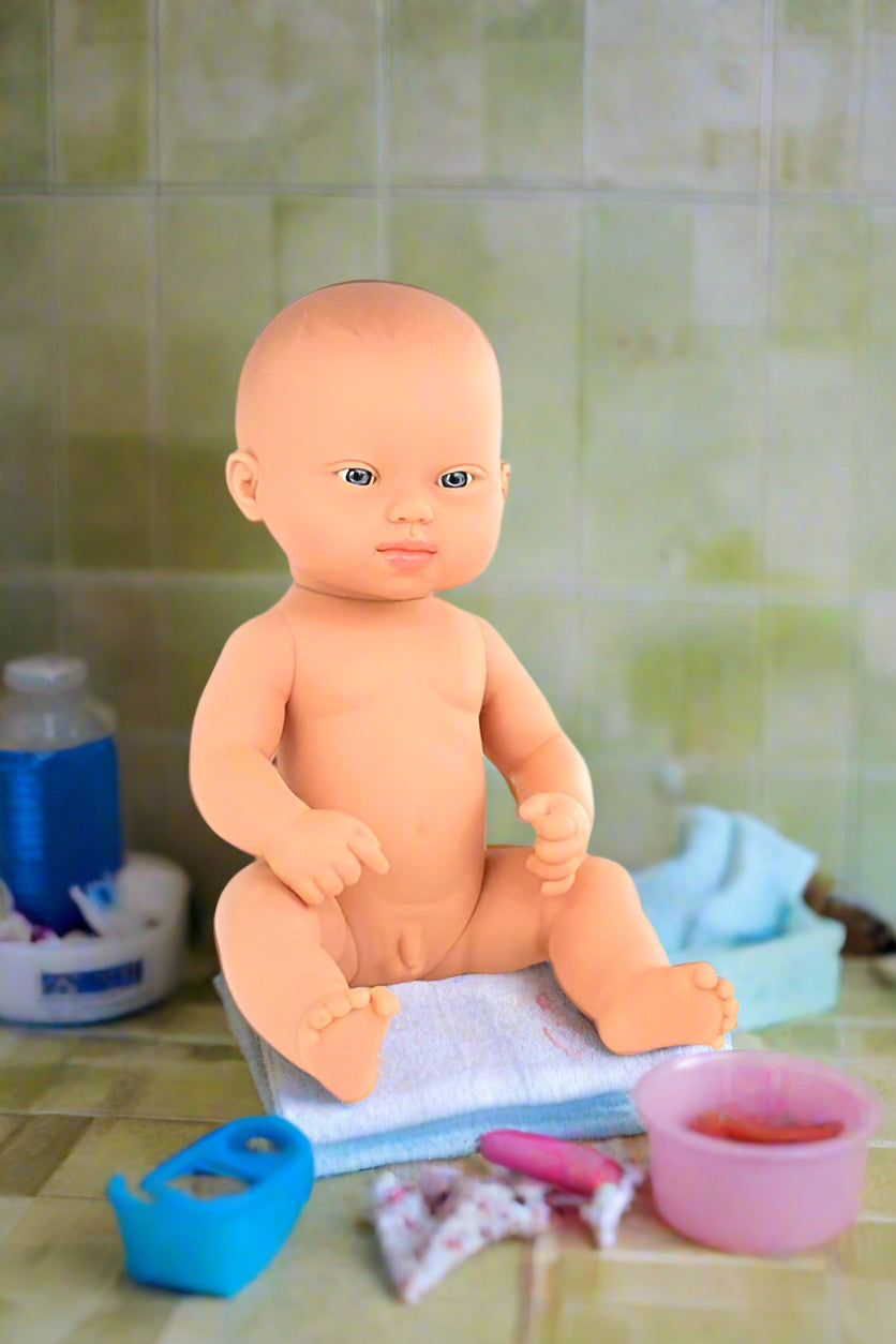 Anatomically correct Boy Down Syndrome Baby doll sitting on a towel with bathroom items around