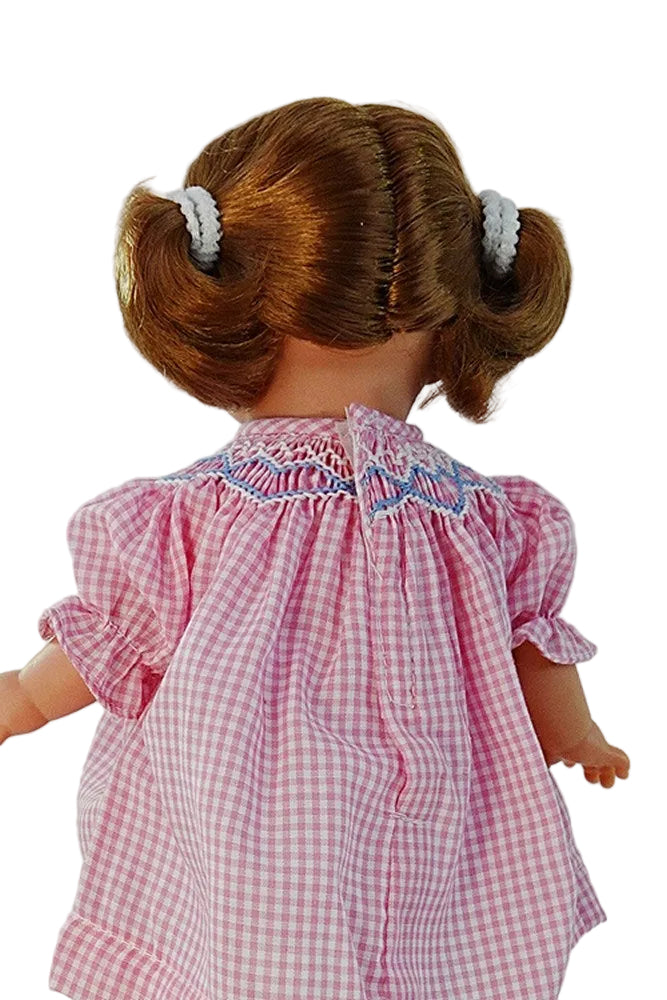 a rear view of our redhead doll showing the hook and loop seam of her pink gingham dress and the smocked and embroidered collar