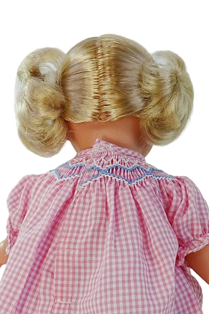 Rear view of blonde doll for young girls showing the hook and loop seam of her hand smocked  pink gingham dress