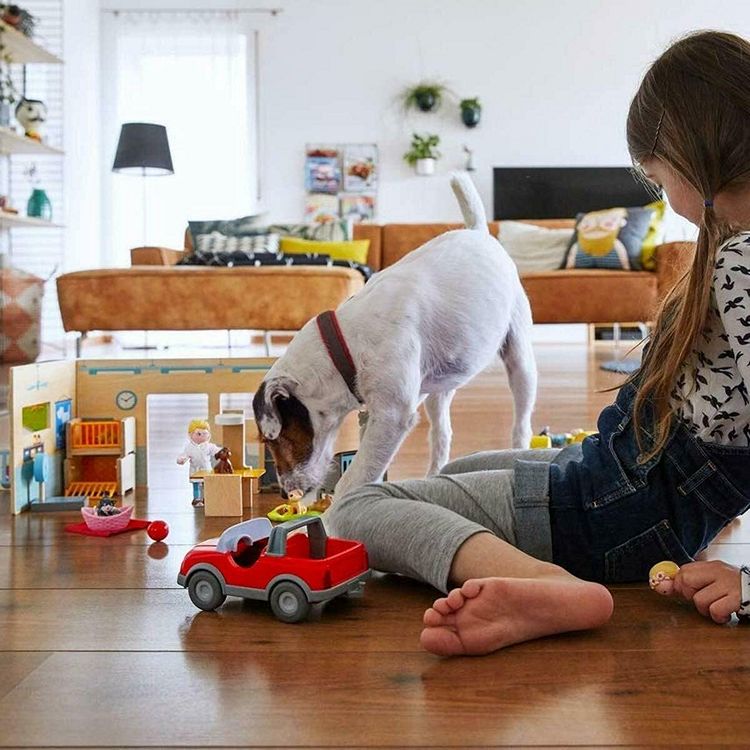 Child with a dog playing on the floor with various toys including dollhouse dolls