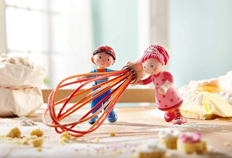  a boy and girl dollhouse dolls dusted in sugar with a whisk on a kitchen counter.
