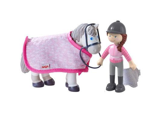 HABA toy horse with pink blanket and HABA logo, standing next to a toy figure of a girl in equestrian attire on a white background.