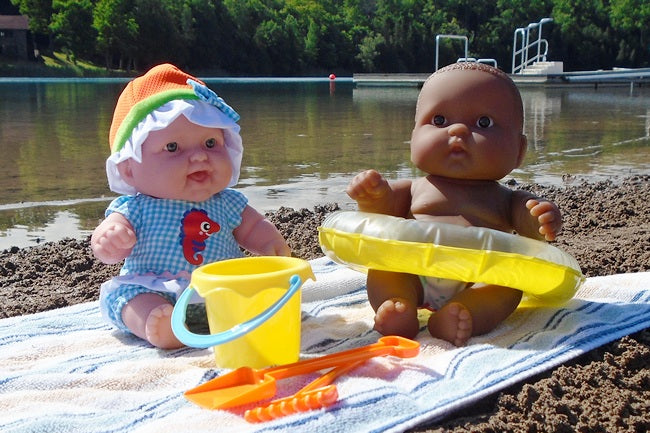 Two dolls with beach accessories on a towel by a lake