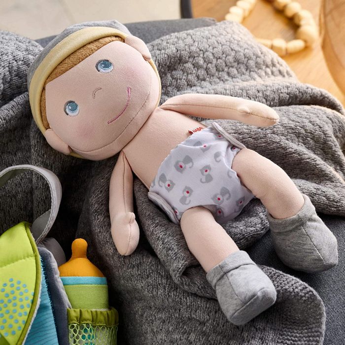Plush Maxine baby doll with a diaper on a gray blanket with toys around