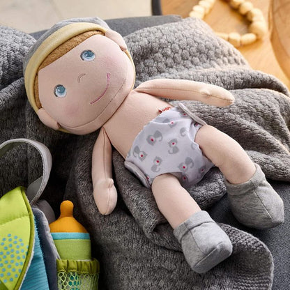 Plush Maxine baby doll with a diaper on a gray blanket with toys around