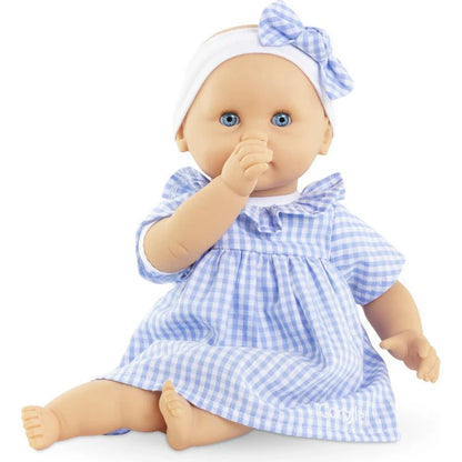 Corolle Calin Milly soft body baby doll seated with hand raised to mouth showing sweet curious expression in blue gingham dress