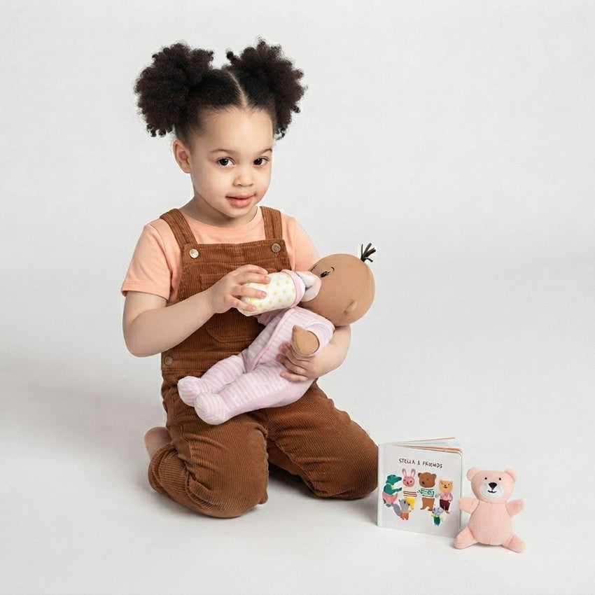 A biracial toddler girl feeding her baby stella biracial doll a pretend bottle