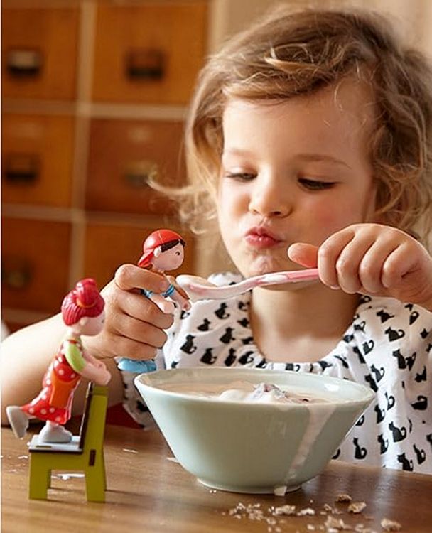 Child pretend feeding dollhouse dolls with her own spoon and cereal bowl