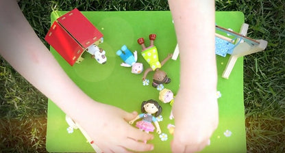 A young child playing with several of the HABA Dollhouse dolls and playsets