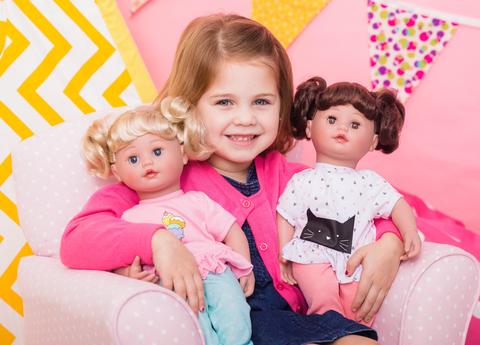 a young girl holding the blonde and brunette versions of the Cuddle & Coo dolls