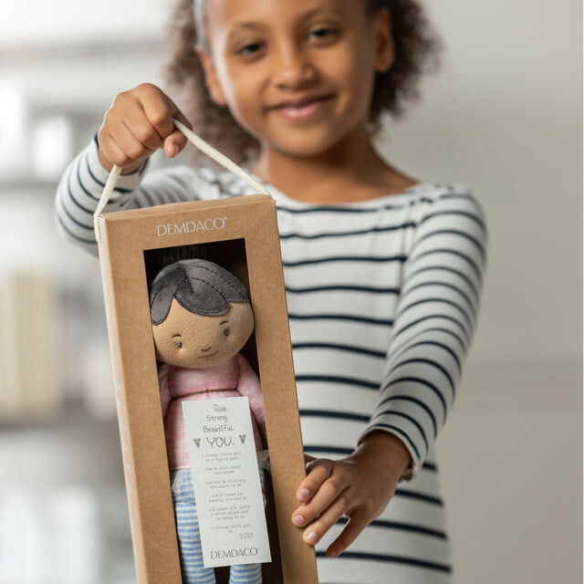 A young girl holding a demdaco strong beautiful you ethnic rag doll