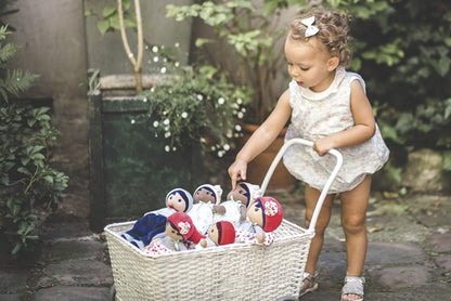A toddler pushing a stroller with an assortment of Kaloo cloth rag dolls